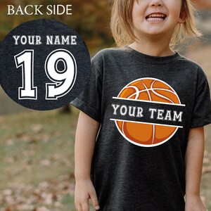 May include: A dark gray t-shirt with a basketball graphic and the text "YOUR TEAM". The basketball is orange and brown with white lines. The number 19 is on the back of the shirt.