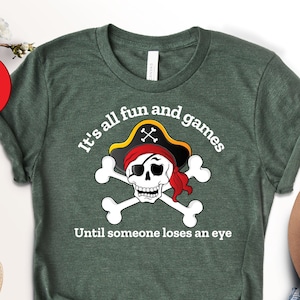 May include: A green t-shirt with a white skull and crossbones graphic. The skull is wearing a red bandana and a black pirate hat. The text on the shirt reads "It's all fun and games until someone loses an eye."