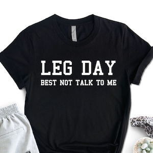 May include: Black t-shirt with white text that reads "LEG DAY BEST NOT TALK TO ME".
