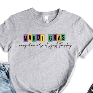 May include: Gray t-shirt with the text "Mardi Gras" in colorful block letters and the text "everywhere else it's just Tuesday" in black script.