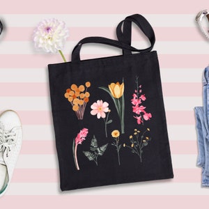 May include: A black canvas tote bag with a floral design. The flowers are pink, orange, and yellow. The bag has two handles.