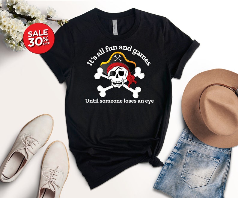May include: Black t-shirt with a white skull and crossbones graphic. The skull is wearing a red bandana and a pirate hat. The text "It's all fun and games Until someone loses an eye" is printed below the graphic.