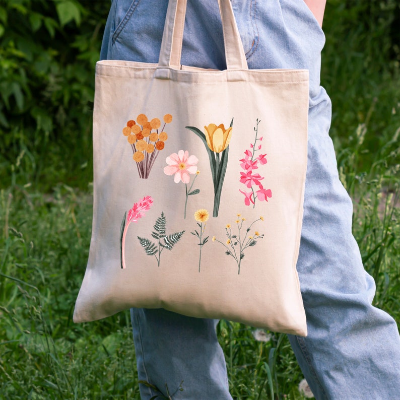 May include: A beige tote bag with a floral design. The flowers are yellow, pink, and orange. The bag has a long handle.