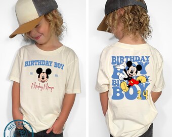 May include: Off-white t-shirt with "BIRTHDAY BOY" in blue, featuring a Mickey Mouse graphic. The front has "Mickey Mouse" in red script. The back has a larger Mickey Mouse and "BOY 14".