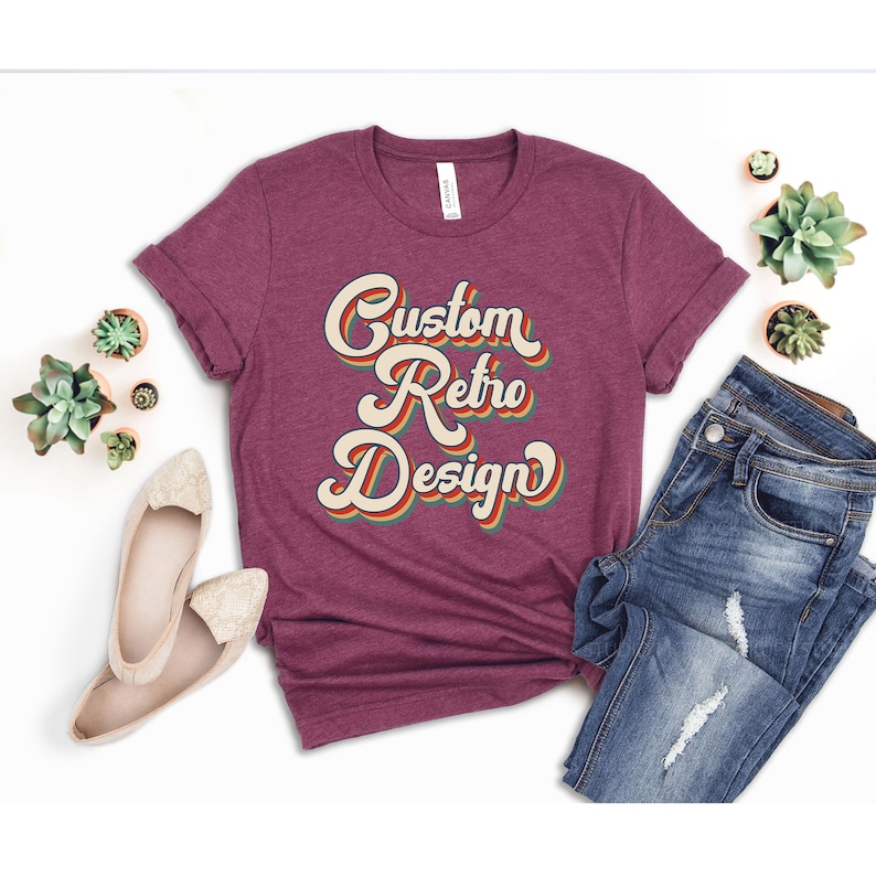 May include: A maroon t-shirt with the text "Custom Retro Design" in a retro font with rainbow colors.