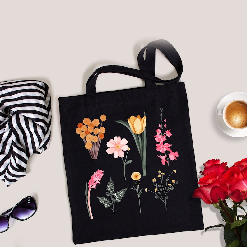 May include: Black tote bag with a floral design featuring pink, orange, and yellow flowers. The bag has a long handle and is made of canvas.
