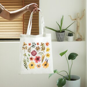 May include: A white tote bag with a floral design. The flowers are in shades of red, orange, yellow, and brown. The bag has two handles and is made of canvas.