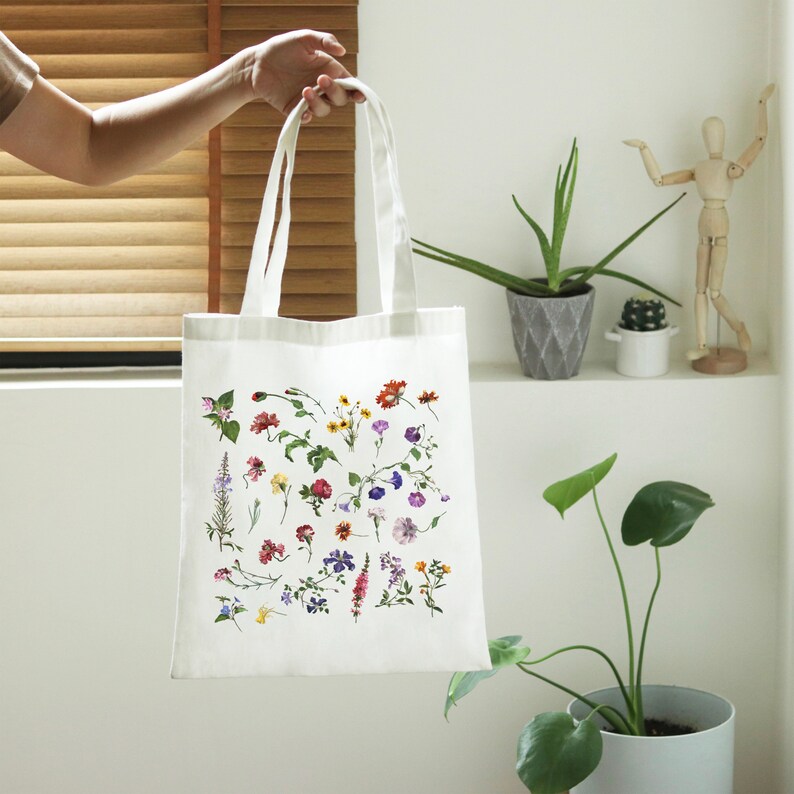 Peut inclure: Sac fourre-tout en toile blanche avec un imprim&eacute; floral pr&eacute;sentant une vari&eacute;t&eacute; de fleurs color&eacute;es. Le sac a deux anses et est fait d'un mat&eacute;riau durable.