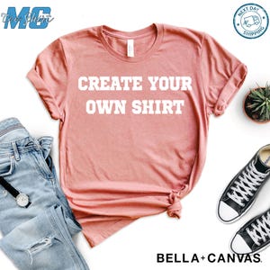 Puede incluir: Camiseta de color rosa polvoriento con el texto blanco "CREATE YOUR OWN SHIRT". La imagen incluye vaqueros azules, un reloj y zapatillas de lona negras. La camiseta es de Bella + Canvas.