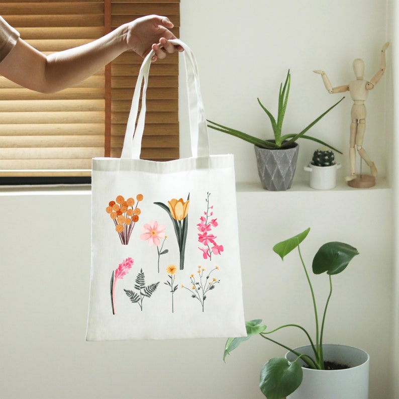 May include: White canvas tote bag with a floral design featuring pink, yellow, and orange flowers. The flowers are illustrated in a simple, modern style.