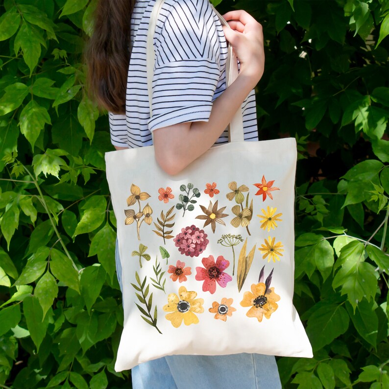 May include: A white canvas tote bag with a floral design. The flowers are in shades of yellow, orange, red, and pink. The bag has two long handles.