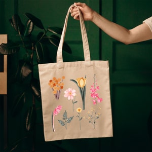 May include: A beige canvas tote bag with a floral design. The flowers are pink, yellow, and orange. The bag has two long handles.