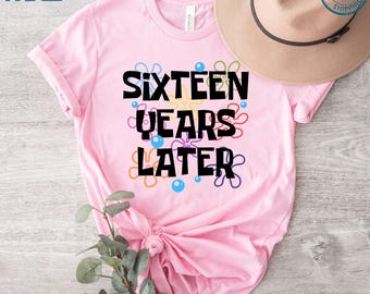 May include: Pink t-shirt with the text "Sixteen Years Later" in black lettering. The text is surrounded by colorful cartoon-style flowers.