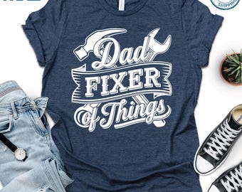 May include: A navy blue t-shirt with a white graphic design that says "Dad Fixer of Things". The graphic includes a hammer and wrench.
