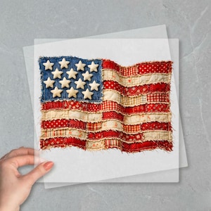 May include: A handcrafted American flag made of fabric. The flag features a blue denim field with white stars and red and white striped sections. The flag is held on a white surface.