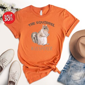 May include: Orange t-shirt with a watercolor illustration of a squirrel and the text "The Squirrel Whisperer".