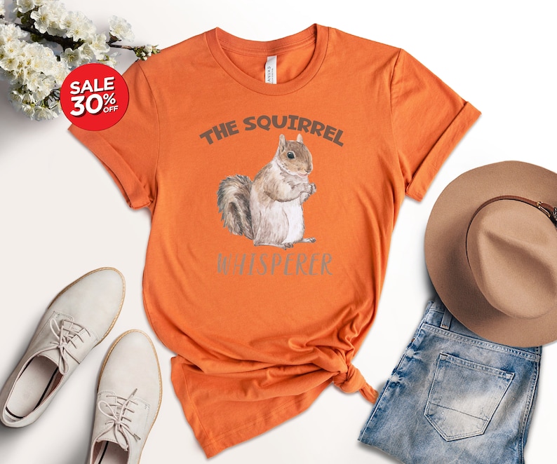 May include: Orange t-shirt with a watercolor illustration of a squirrel and the text "The Squirrel Whisperer".