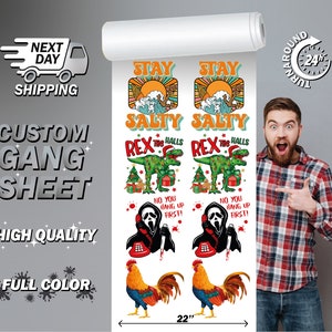 May include: A sheet of iron-on transfer designs featuring a variety of holiday-themed images, including a rooster, a ghost on a phone, a dinosaur, and a sunset with the text "Stay Salty". The sheet is 56 cm wide and includes the text "Custom Gang Sheet, High Quality, Full Color".
