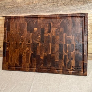 May include: A large, rectangular, wooden cutting board made of dark brown wood with a checkered pattern. The board has a beveled edge and a small logo that reads "Kaga & Co."