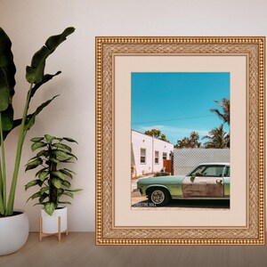May include: A framed photograph of a vintage green car parked in front of a white house with a blue sky and palm trees in the background. The photo is signed "Christine Hall".