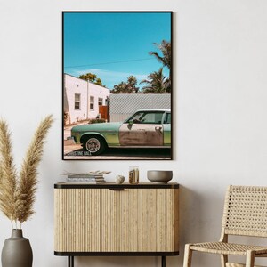 May include: A vintage green car parked in front of a white building with a blue sky and palm trees in the background. The car has a dented door and a faded paint job. The image is titled "Christine Hall".