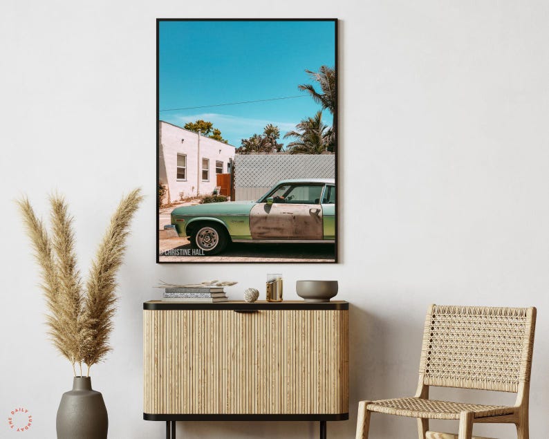 May include: A vintage green car parked in front of a white building with a blue sky and palm trees in the background. The car has a dented door and a faded paint job. The image is titled "Christine Hall".