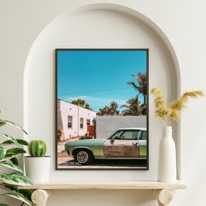 May include: A vintage green car parked in front of a white building with a blue sky and palm trees in the background. The car has rust on the side and the text "CHRISTINE HALL" is visible on the bottom of the image.