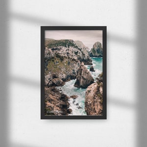 May include: A photograph of a rocky coastline with turquoise water crashing against the rocks. The image is taken from a high vantage point, looking down at the water and the cliffs. The sky is overcast and the water is choppy.