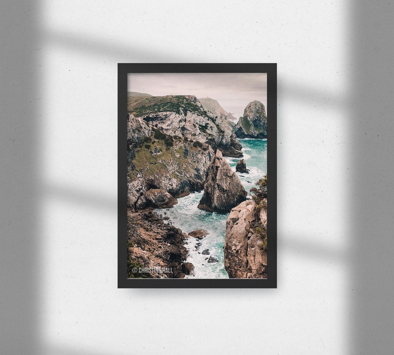 May include: A photograph of a rocky coastline with turquoise water crashing against the rocks. The image is taken from a high vantage point, looking down at the water and the cliffs. The sky is overcast and the water is choppy.