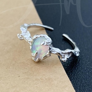 Op de afbeelding: Een zilveren ring met een witte opaal-edelsteen gezet in een takvormig ontwerp.