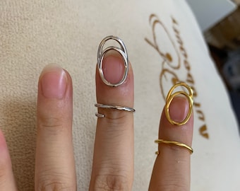 May include: Two rings, one silver and one gold, are worn on the index and middle fingers of a hand. Both rings are open circle designs with a smaller circle inside the larger circle.