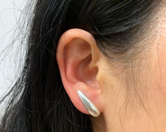 May include: A pair of silver teardrop-shaped earrings. The earrings are worn in the earlobes of a person with dark hair.