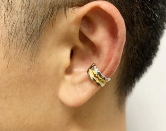 Könnte beinhalten: Ein silberner und goldener Ohrklemmen-Schmuck wird am Ohr getragen. Der Schmuck hat ein strukturiertes, organisches Design mit einer silbernen Basis und goldenen Akzenten. Es ist ein Ohrschmuck.