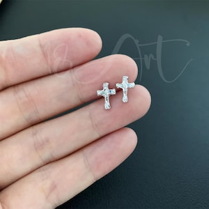 May include: A pair of silver cross earrings with clear cubic zirconia stones. The earrings are small and delicate.