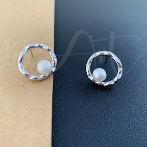 May include: A pair of silver earrings with a textured circular design and a small white pearl in the centre of each circle.