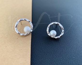 May include: A pair of silver earrings with a textured circular design and a small white pearl in the center of each circle.