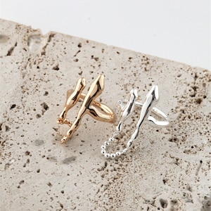May include: Two abstract rings with a chain detail. The ring on the left is gold and the ring on the right is silver.