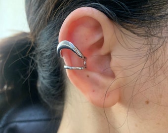 Puede incluir: Un pendiente de oreja de plata con un diseño curvo. El pendiente se lleva en la parte superior de la oreja.