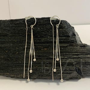 Könnte beinhalten: Ein Paar silberne Ohrringe mit drei kleinen silbernen Perlen an jedem Ohrring.