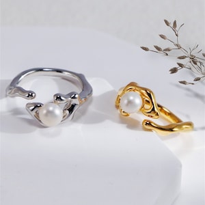 Puede incluir: Dos anillos ajustables con un acento de perla. El anillo de la izquierda es de plata y el anillo de la derecha es de oro.