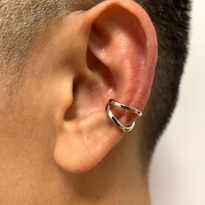 May include: A silver ear cuff with a double-band design. The cuff is worn on the upper ear and has a smooth, polished finish. The jewelry is a modern accessory.