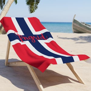 May include: A beach chair with a red, white, and blue beach towel featuring the Norwegian flag and the name "Ingrid" written in red.