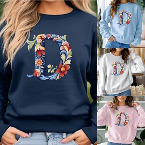 Könnte beinhalten: Ein marineblauer Sweatshirt mit einem floralen Design des Buchstabens "D" auf der Vorderseite.