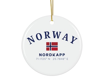 May include: A white ceramic ornament with a gold string for hanging. The ornament features the word "NORWAY" in navy blue, a Norwegian flag, and the text "NORDKAPP" with coordinates.