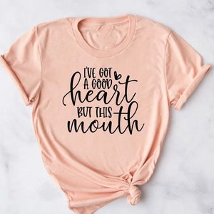May include: A peach-colored t-shirt with a black graphic that reads "I've got a good heart but this mouth".