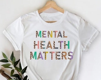 May include: White t-shirt with the text "MENTAL HEALTH MATTERS" in colourful letters with a leopard print pattern.