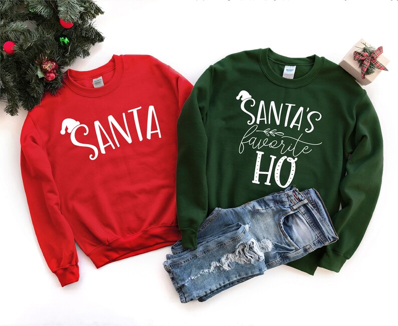May include: Two crew neck sweatshirts. One is red with the word "SANTA" in white, and the other is dark green with the text "SANTA'S favorite HO" in white. A pair of blue denim shorts is placed between the sweatshirts.