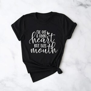 May include: Black t-shirt with a white graphic that says "I've got a good heart but this mouth".