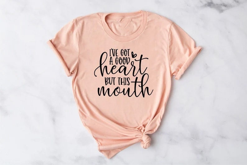 May include: A peach-colored t-shirt with a black graphic that reads "I've got a good heart but this mouth".
