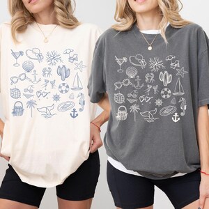 Two women wearing t-shirts with various beach and nautical-themed illustrations.